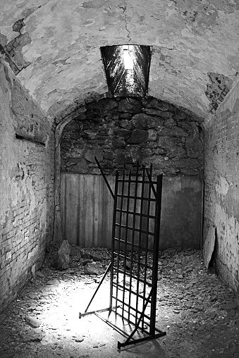 An old bed frame stands in the middle of a prison cell.