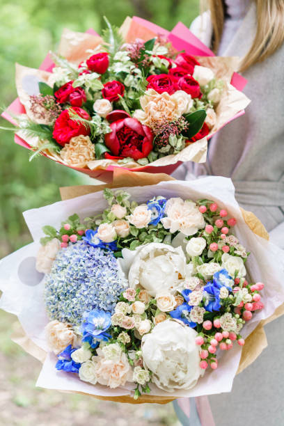 istock Young girl holding two a beautiful spring bouquets. flower arrangement with hydrangea and peonies. Color light blue and red. The concept of a flower shop, a small family business 985208812
