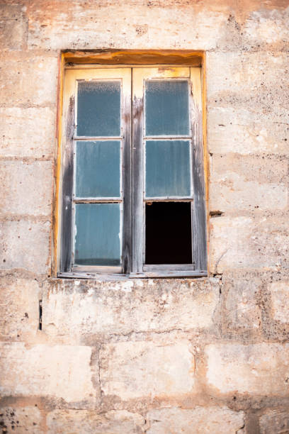 istock Old window with broken glass in limestone wall. 985237602