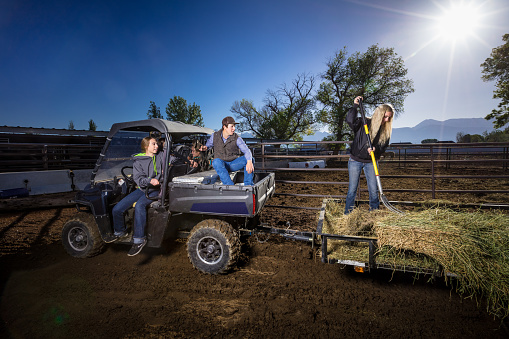 Dramatic portrait of a group of young people posing on a UTV and a hay-filled trailer, shot with artificial light on location at a ranch in Utah, USA.