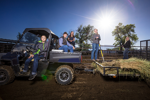 Dramatic portrait of a group of young people posing on a UTV and a hay-filled trailer, shot with artificial light on location at a ranch in Utah, USA.