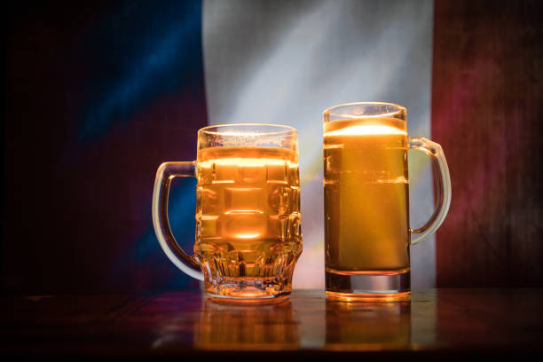 istock Creative concept. Beer glasses on table at dark toned foggy background with blurred view of flag of France. Support your country with beer concept. 985246228