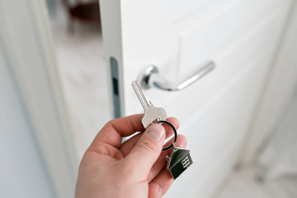 istock Mortgage concept. Men hand holding key with house keychain. Modern light lobby interior. Real estate, moving home or renting property. 985259722