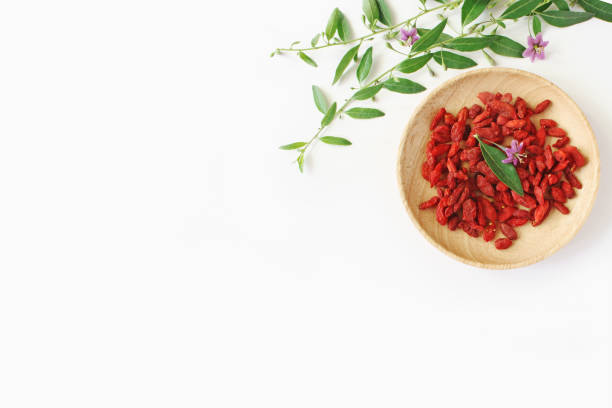 Heap of dried Goji berries fruit, Lycium barbarum in wooden bowl on white table. Blossoming wolfberry herbal plant branch. Healthy superfood. Flatlay, top view. Heap of dried Goji berries fruit, Lycium barbarum in wooden bowl on white table. Blossoming wolfberry herbal plant branch. Healthy superfood, flatlay, top view. wolfberry berry berry fruit red stock pictures, royalty-free photos & images