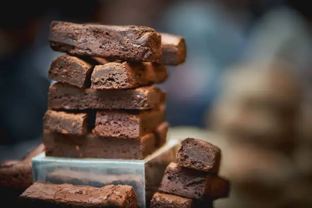 Photo of Stack of chocolate brownies with a blurred background on sale in bakery stall in a food market.