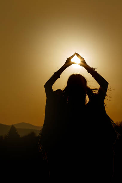 silhouette der frau händen mit sonne im dreieck am hintergrund der schönen sonnenuntergang - heaven women sunrise inspiration stock-fotos und bilder