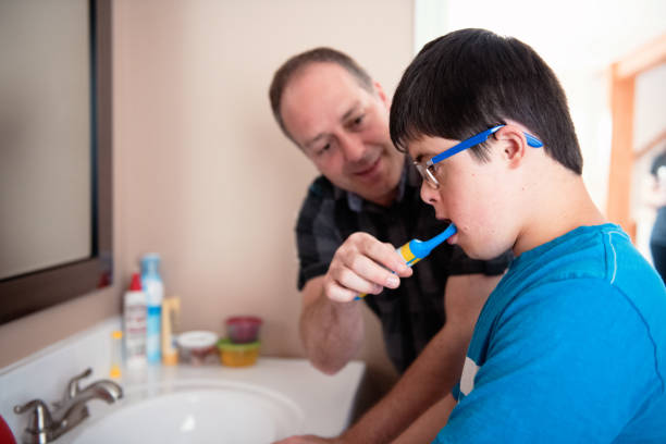 Father helping her son of 12 years old with Autism and Down Syndrome in daily lives brushing her teeth stock photo
