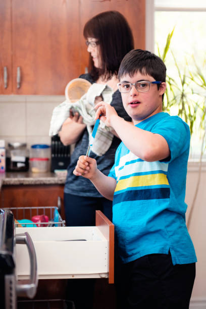 mother helping her son of 12 years old with autism and down syndrome in daily lives emptying the dishwasher - independence lifestyles smiling years imagens e fotografias de stock