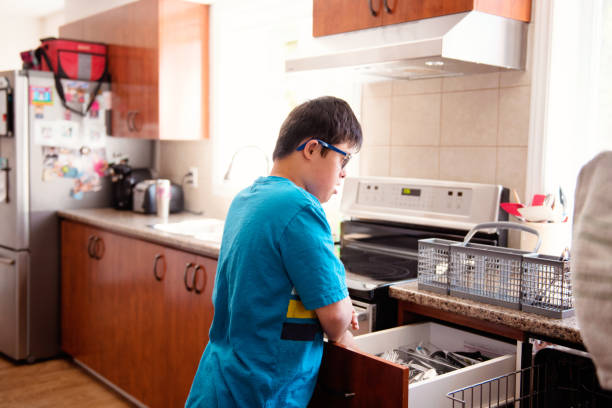 mother helping her son of 12 years old with autism and down syndrome in daily lives emptying the dishwasher - independence lifestyles smiling years imagens e fotografias de stock