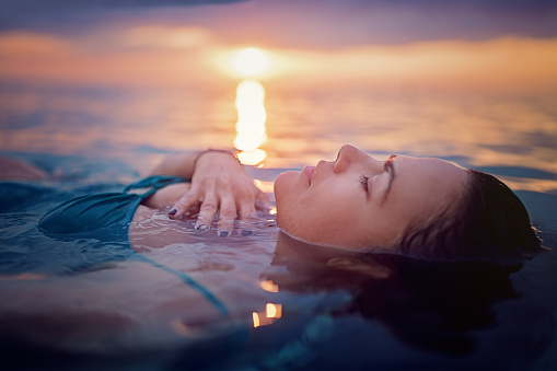 Woman is lying and relaxing in the ocean at the front of a beautiful sunset