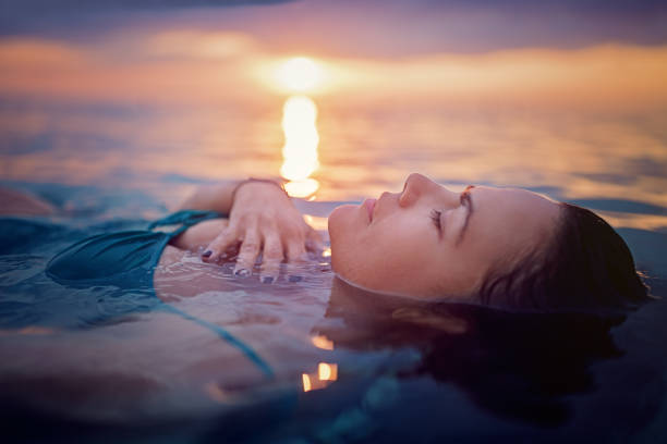 woman is lying and relaxing in the ocean at the front of a beautiful sunset - earth globe mother child imagens e fotografias de stock