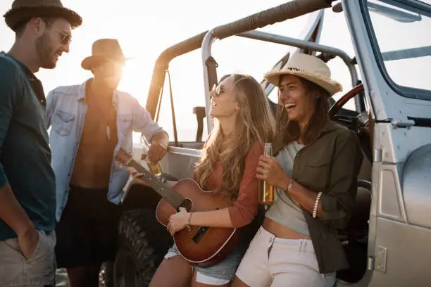 Friends enjoying springbreak at the beach playing a guitar by the car