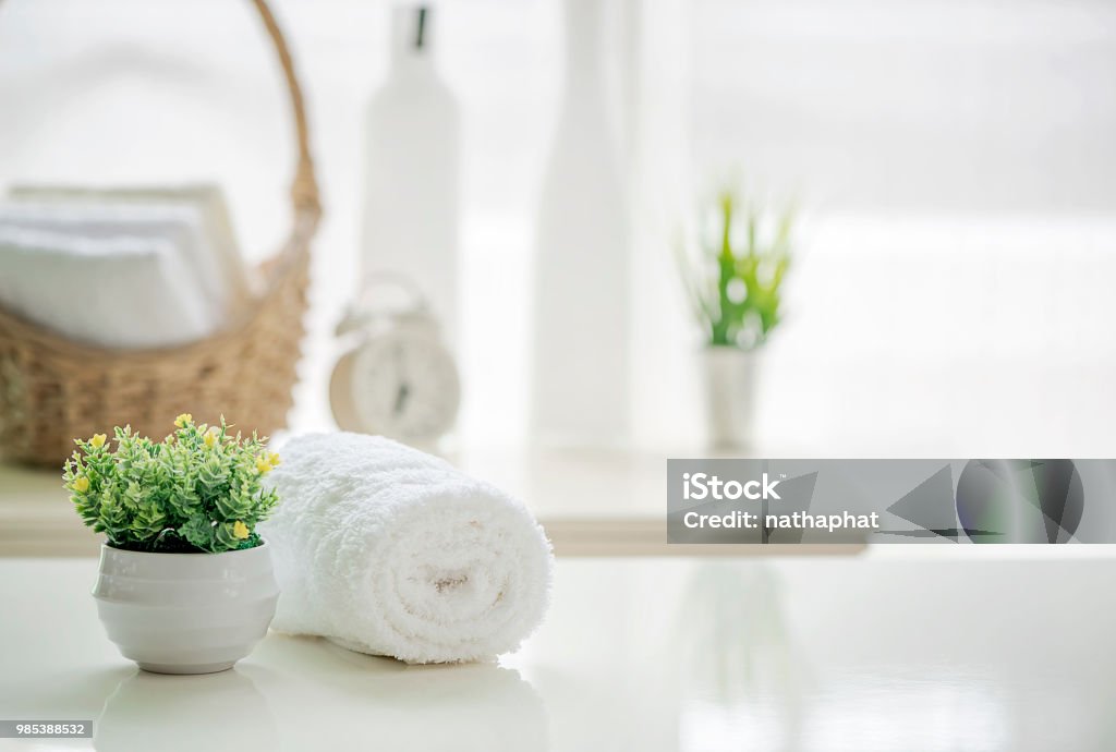 Roll up of white towels on white table with copy space on blurred living room background Roll up of white towels on white table with copy space on blurred living room background. For product display montage. Spa Stock Photo