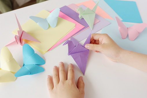 Children's hands do origami from colored paper on white background. lesson of origami