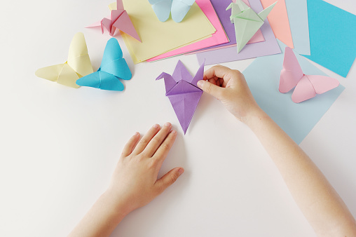 Children's hands do origami from colored paper on white background. lesson of origami