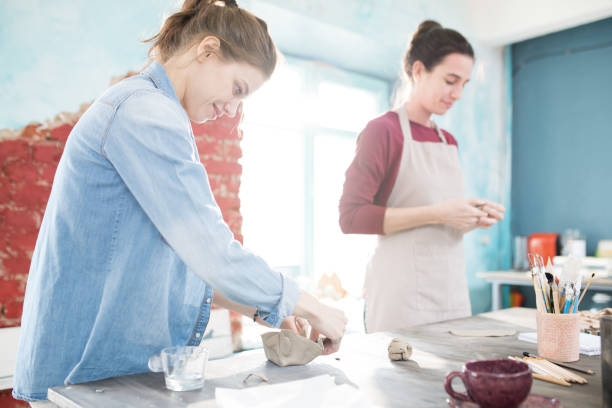 istock Positive pretty young woman learning sculpting and making crockery from clay enjoying process at pottery class 985518744