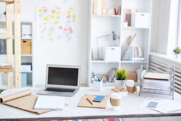 Modern marketers workplace with small laptop, container for files, sketchpads, coffee cups and office supplies