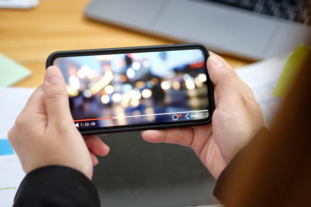 istock Close up of women's hands holding mobile phone while play video from network in office. 985545300