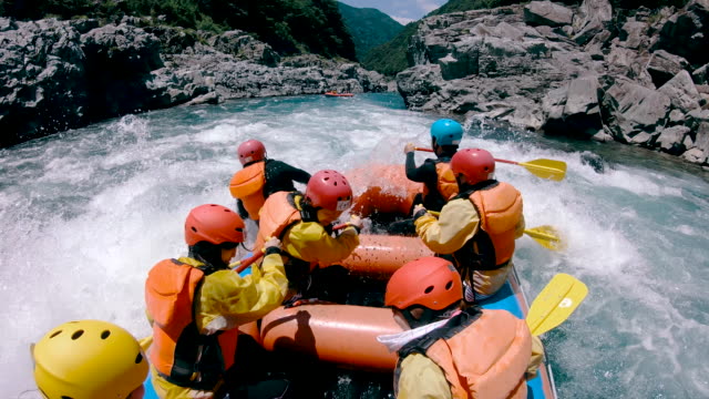 Small group of men and women white water river rafting in a forested valley in Japan.