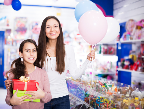 Portrait of cheerful mother and daughter holding gifts and balloons in store