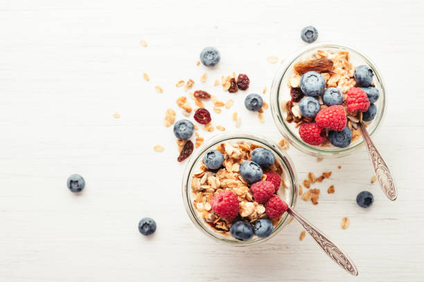 Granola with berries and yogurt in jars. Two jars with granola, berries and yogurt on white wooden table. Top view. parfait stock pictures, royalty-free photos & images