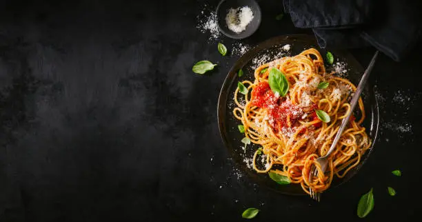 Tasty appetizing classic italian spaghetti pasta with tomato sauce, cheese parmesan and basil on plate on dark table. View from above, horizontal