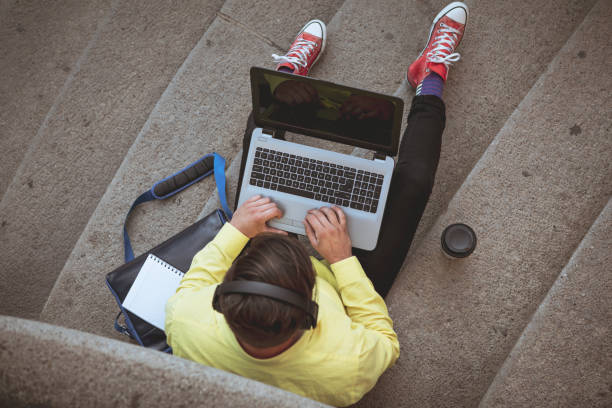 Young hipster man working on laptop while sitting on the stairs.