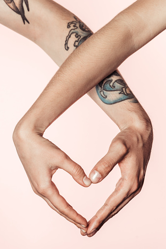 partial view of woman and tattooed man doing heart symbol by hands isolated on pink background