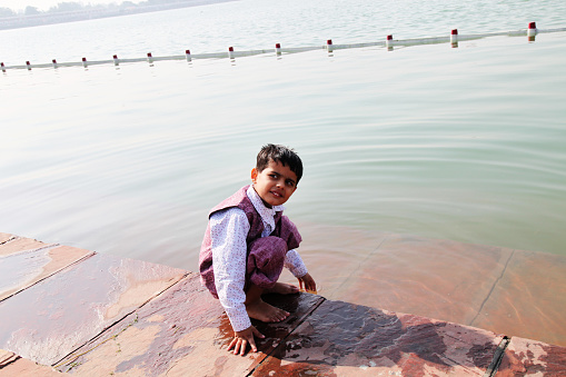 Elementary age boy sitting portrait near brahma sarovara in holy land of kurukshetra during casual festival.