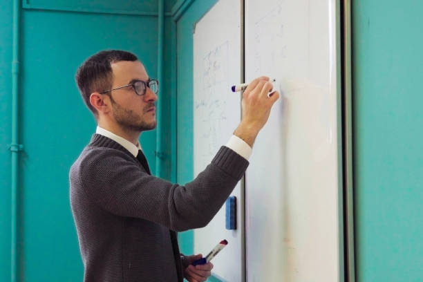 istock Man teacher in glasses writes on whiteboard in classroom 985749662