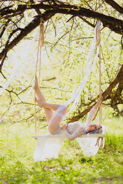 istock Young bride in white negligee laying on a swing in seductive pose 985749762