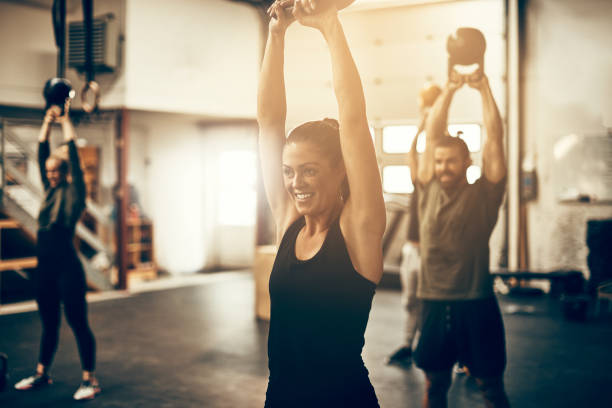 souriante jeune femme balancer un haltère à la salle de gym - human muscle body building muscular build weight training photos et images de collection