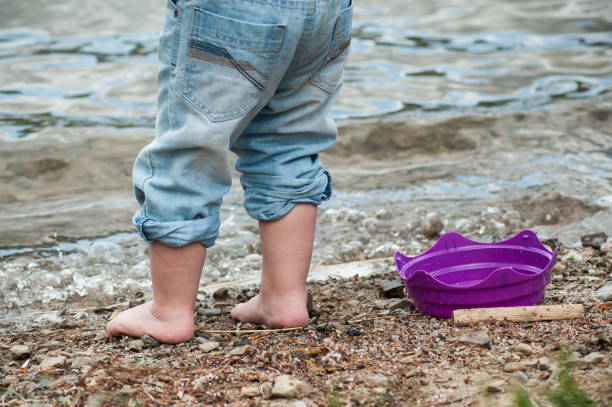 füße des kindes spielen am strand mit kunststoff-spielzeug - child human foot barefoot jeans stock-fotos und bilder