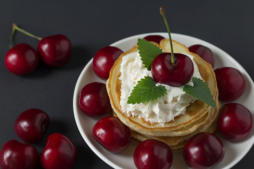 Pancakes with cherries and whipped cream on a black background