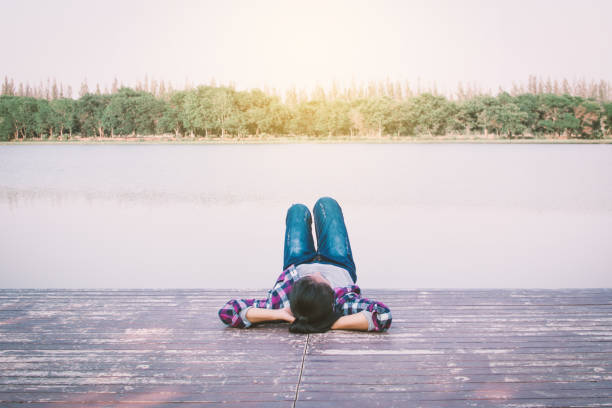 istock Woman Lying Down On Pier Over Lake Against Clear Sky 985786818