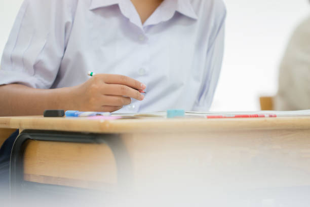 istock Education test concept : Hands Asian students Thai uniform holding pencil for testing exams writing answer sheet or exercise for taking fill in exam paper on row wood table at classroom in high school 985811678