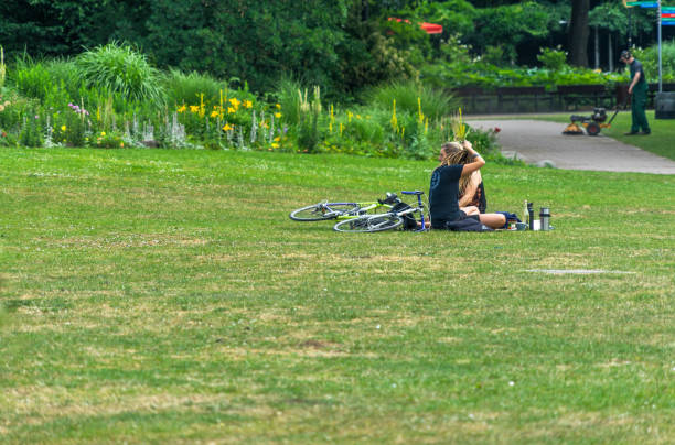 Hamburg, Germany, June 20, 2018: Two students on bicycles taking a lunch break on the lawn of a public park, people