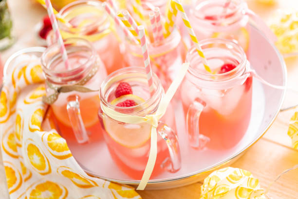 Raspberry lemonade garnished with fresh lemon and raspberries in drinking mason jars.