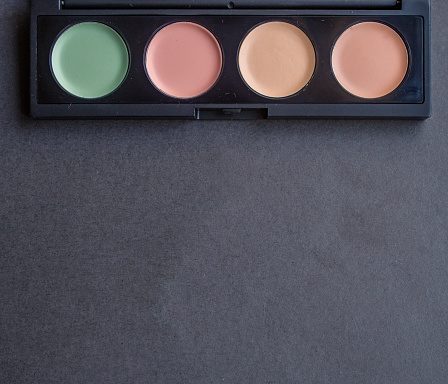Palette with different makeup correctors on black background