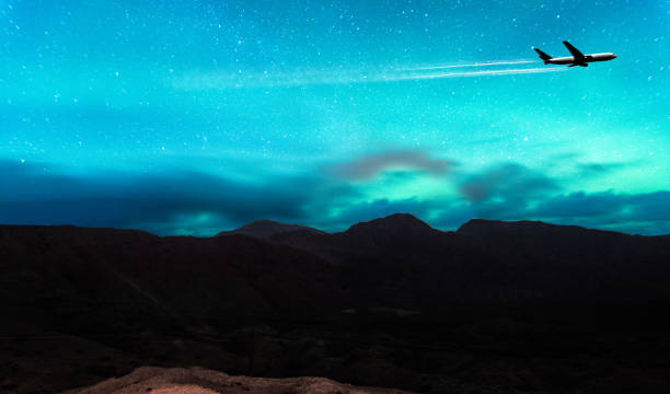 northern lights e silhueta de montanhas com avião e vapor trail passando - aurora borealis iceland astronomy tranquil scene - fotografias e filmes do acervo