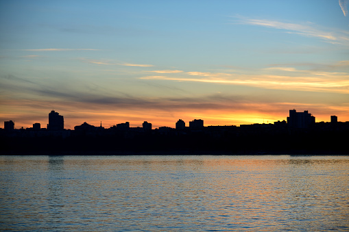 The embankment of the city of Volgograd during sunset. The silhouette of the city on the river during sunset, clear sky, a little feather clouds during sunset over the horizon.