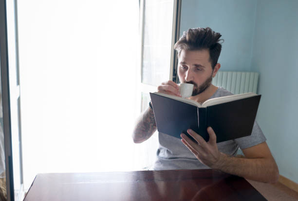 istock Young Man Reading a Book while he drink his coffee 985864628
