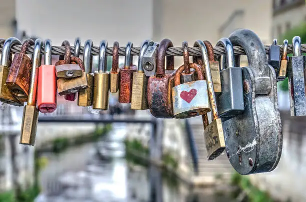 Row of locks attached by couples to the fence of a bridge across the river Geul in Valkenburg, The Netherlands