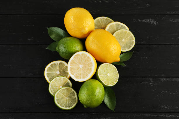 istock Ripe limes and lemons with leafs on black wooden table 985894814