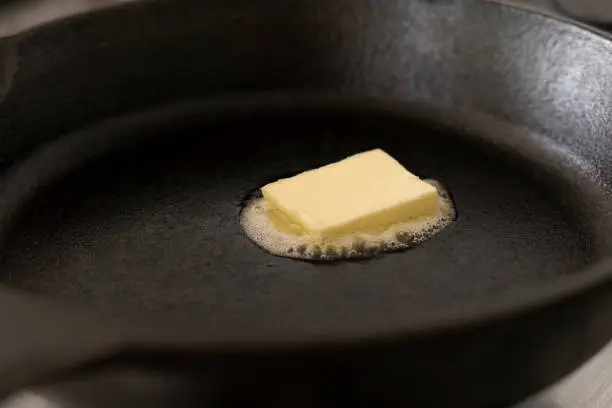 A butter pat melting on a black cast iron frying pan.