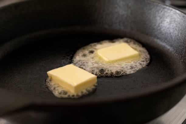 istock Two butter pats  melting on a black cast iron frying pan. 985899174