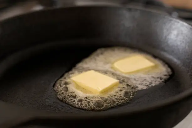 Two butter pats  melting on a black cast iron frying pan.