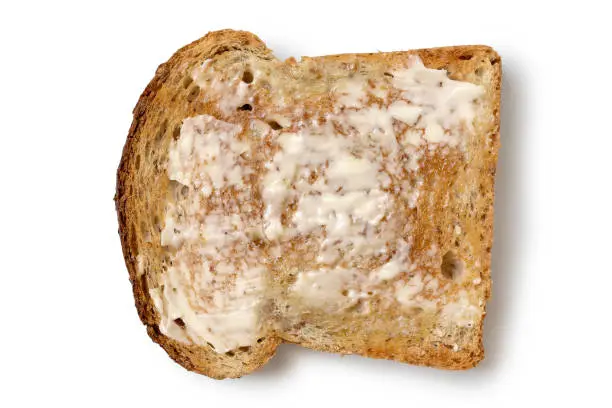 Butter spread on a single slice of whole wheat toast isolated on white from above.
