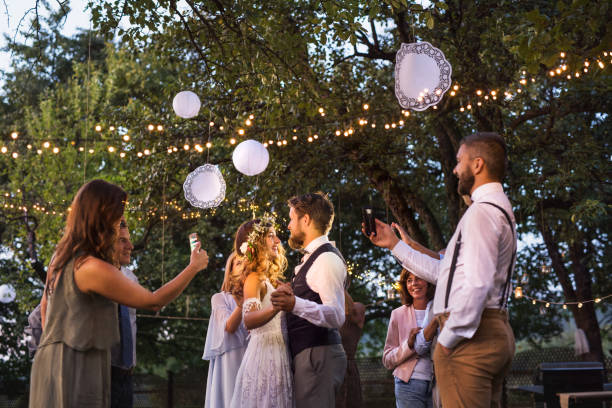 Guests with smartphones taking photo of bride and groom at wedding reception outside. Guests with smartphones taking photo of a dancing bride and groom at wedding reception outside. An evening in the backyard. wedding reception photos stock pictures, royalty-free photos & images
