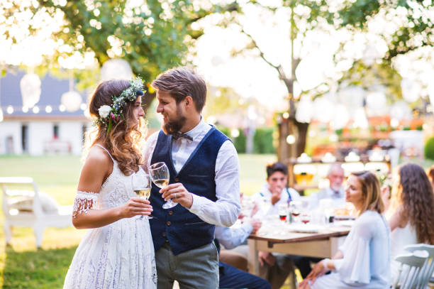 istock Bride and groom clinking glasses at wedding reception outside in the backyard. 985903062
